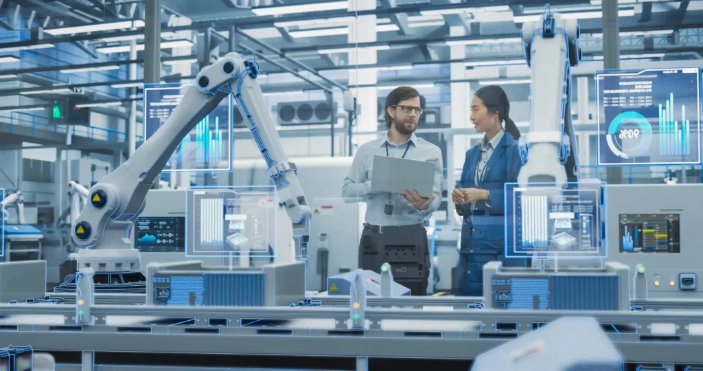 Photo de deux ingénieurs devant une ligne de production équipée d’un bras robotisé et de tableaux de bord